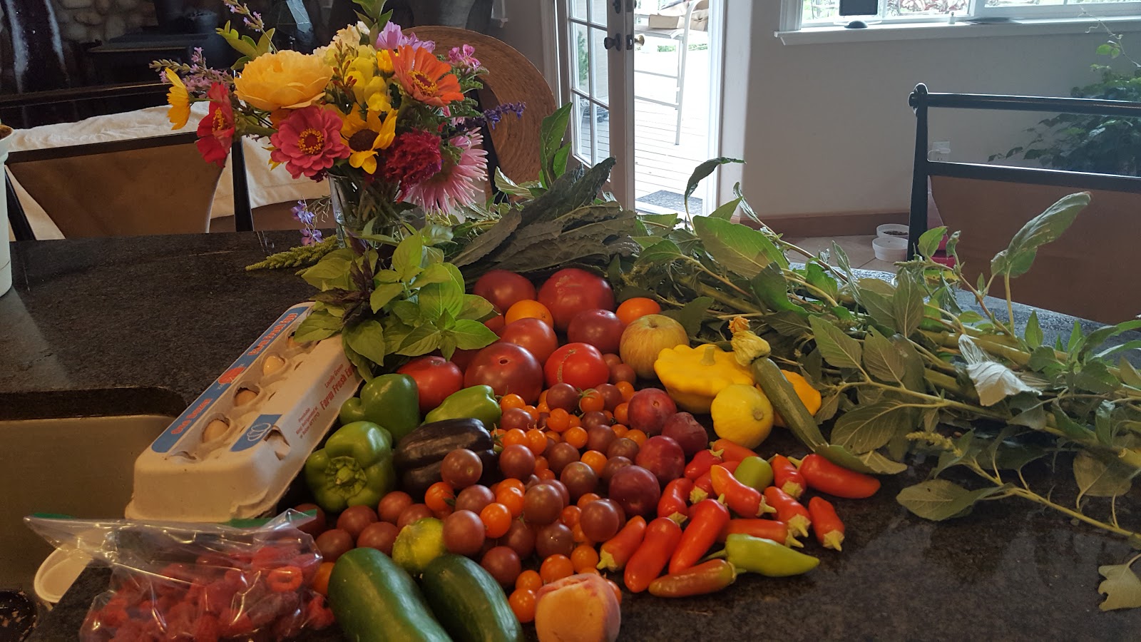 One CSA box laid out: heirloom and cherry tomatoes, peppers, squash, cucumbers, greens, eggs and a jar of cut flowers